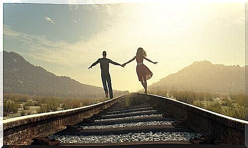 Couple holding hands by the train track to represent idealization