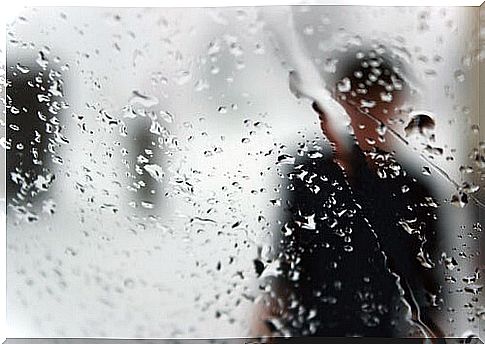 Silhouette of a man behind glass with rain to represent opposite to depression